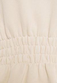 Tela color crema con una cintura texturada y fruncida. Material suave y elástico con un ligero ribeteado, que resalta los detalles elásticos.