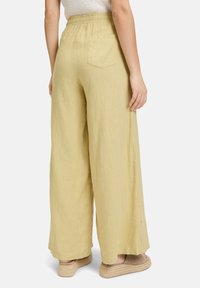Lichtgele linnen wijde broek met een elastische tailleband, zijsplitten en een achterzak, weergegeven vanuit het achteraanzicht.