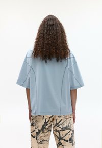 Světlomodré oversized tričko s kulatým výstřihem a krátkými rukávy, doplněné béžovými kalhotami s tmavým, abstraktním vzorem větví.