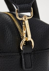 Črna usnjena torbica z teksturno površino, opremljena z zlatim zadrgo in kovinskimi dodatki. Zaponka zadrge je gravirana z "VALENTINO."