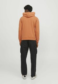 Sudadera con capucha en naranja apagado, con un corte relajado. Combinada con pantalones cargo negros, que muestran bolsillos funcionales y una silueta suelta.