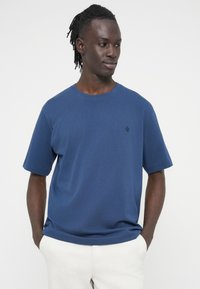 Μπλε ναυτικό βαμβακερό t-shirt με κοντά μανίκια, λαιμόκοψη σε σχήμα κύκλου και διακριτικό κεντημένο λογότυπο στο στήθος. Λεία υφή, άνετη γραμμή.