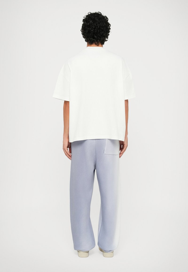 White oversized t-shirt with short sleeves, paired with loose, light blue sweatpants featuring a back pocket and ribbed cuffs.