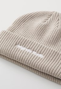Beige gebreide beanie met ribbelstructuur. Voorzien van een wit "Originals Studio" logo aan de voorkant. Zacht en flexibel ontwerp.