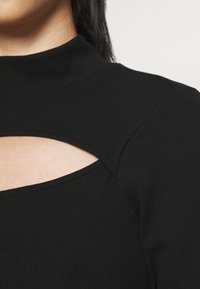 Black ribbed long-sleeve top featuring a cutout detail beneath the neck. The fabric has a smooth texture with a stretch fit.