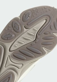 Semelle de chaussure en gris clair avec un caoutchouc texturé et des motifs ovales et circulaires variés pour l'adhérence. Design courbé pour la flexibilité et le soutien.