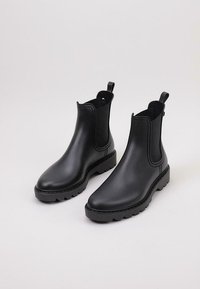 Botas negras, de altura hasta el tobillo, con un acabado suave y brillante, paneles laterales elásticos y una suela de goma texturizada para mayor tracción.