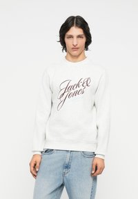 Sudadera gris claro con cuello redondo, que presenta el texto en cursiva oscuro "Jack & Jones" en el pecho, puños y dobladillo acanalados.