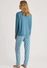 Blauwe lange mouwen top gecombineerd met lichtblauwe broek met een diamanten patroon in wit en roze. Zachte stof met een relaxte pasvorm.