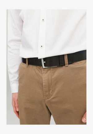 Pantalon en tissu marron associé à une ceinture en cuir noir avec une boucle en métal argenté, porté avec une chemise blanche à boutons.