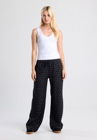 Black polka dot pants with an elastic waistband and side pockets, paired with a fitted white V-neck tank top. Lightweight fabric, relaxed fit.