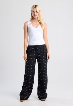 Black polka dot pants with an elastic waistband and side pockets, paired with a fitted white V-neck tank top. Lightweight fabric, relaxed fit.
