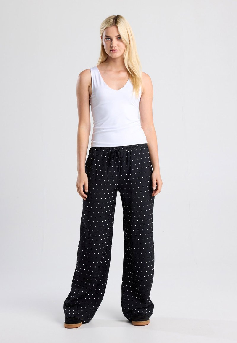 Black polka dot pants with an elastic waistband and side pockets, paired with a fitted white V-neck tank top. Lightweight fabric, relaxed fit.