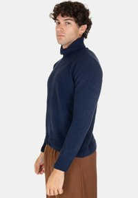 Maglione a collo alto blu navy in un morbido tessuto testurizzato, con polsini e orlo a coste. Design aderente, mostrato su un modello di lato.