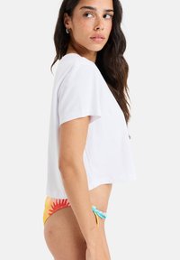 White cropped t-shirt with short sleeves, paired with colorful patterned bikini bottom featuring floral designs and ties at the sides.