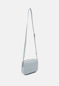 Světlomodrá kabelka přes rameno vyrobená z prošívané kůže, s obdélníkovým tvarem, zipovým zavíráním a nastavitelným popruhem se stříbrným kováním.
