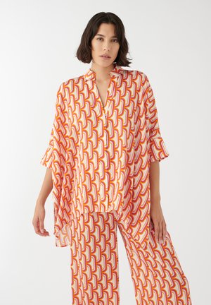 Večbarvna bluza in hlače, okrašeni s geometrijskim vzorcem v rdečih, oranžnih in rumenih odtenkih; lahkoten material in ohlapen kroj.