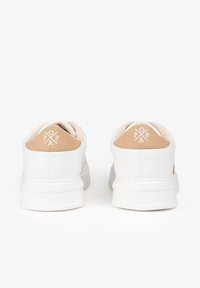 Zapatillas blancas con una pestaña de talón de ante marrón texturizado, diseño minimalista, punta redonda y detalle del logo en la parte trasera.