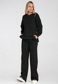 Czarny sweter z luźnym krojem i długimi rękawami, w połączeniu z pasującymi czarnymi spodniami o szerokich nogawkach. Oba wykonane z miękkiego, gładkiego materiału.