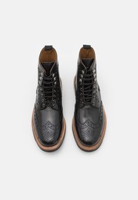 Botas de cuero negro con cordones y detalles de brogue, puntera redonda y suela de marrón claro. Presenta ojales de metal y un acabado texturizado.