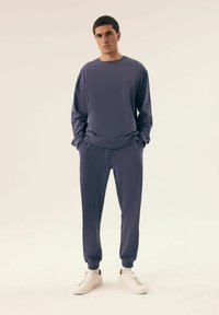 Fioletowy sweter i dopasowane dresy z prążkowanymi mankietami, wykonane z miękkiego materiału; białe sneakersy dopełniają strój.