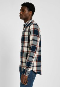 Camicia a maniche lunghe a scacchi nei colori blu navy, rosso, grigio e crema. Realizzata in un tessuto morbido, presenta una tasca sul petto e polsini abbottonati.