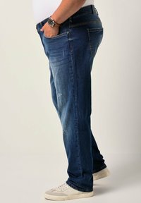 Jeans de mezclilla azul oscuro con un diseño de pierna recta, que presentan acentos desgastados y bolsillos laterales, combinados con zapatillas blancas.