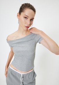 Harmaa ribattu olkaimeton paita lyhyillä hihoilla, vartalonmyötäinen malli ja pehmeä materiaali; yhdistettynä harmaisiin raidallisiin nyörihousuihin.