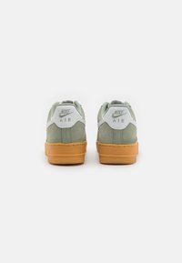 Nike Air tornacipő, puha zöld velúr felsőrésszel, fehér kiegészítőkkel és gumírozott talppal. A sarokon domború logó található.