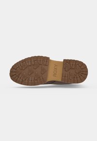 Semelle de chaussure marron avec des crampons profonds, des motifs triangulaires, et le nom de la marque Roxy embossé au centre.