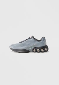 Chaussure de sport grise avec un dessus en maille texturée, semelle noire et accents métalliques. Présente un design de rembourrage unique avec des éléments arrondis.
