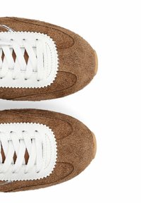 Baskets marron texturées avec des lacets blancs et un détail en cuir, vues de dessus sur un fond blanc.