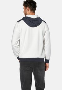 Weißer Kapuzenpullover mit navy Kapuze, gerippten Bündchen und Saum. Glatte Textur, lockere Passform und kontrastierende Schulterdetails.