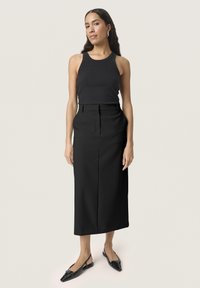 Top in cotone a coste nera abbinato a una gonna midi nera a tubino, che mette in mostra una texture liscia e una vestibilità sartoriale. Le scarpe slingback nere completano l'outfit.