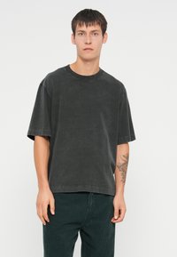 Czarnoszary, oversize t-shirt, krótkie rękawy, okrągły dekolt, miękka bawełniana tkanina, subtelna faktura, w komplecie z zielonymi spodniami z kordurowej tkaniny.