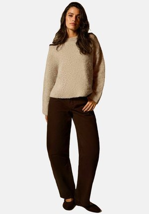 Pull beige clair en peluche avec des manches longues, associé à un pantalon droit marron foncé. Comprend des chaussons noirs. Tenue simple et confortable.