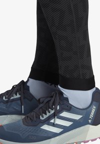 Blue athletic shoes with three white stripes, textured upper, and distinctive sole. Black fitted leggings with a diagonal striped pattern.