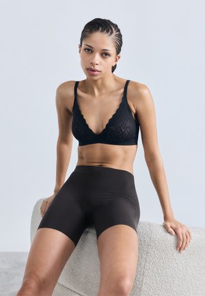 Czarny koronkowy bralet z falistymi krawędziami, zestawiony z wysokim stanem czarnych szortów. Gładka tekstura i bezszwowy design podkreślają dopasowaną sylwetkę.