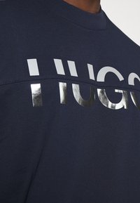 Navy blue cotton sweatshirt featuring a textured silver "HUGO" logo. The design includes a smooth, regular-fit crew neck.