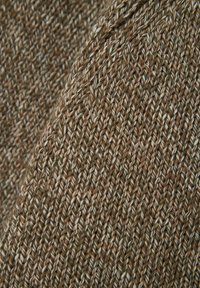 Tessuto lavorato a maglia in toni terrosi di marrone e beige, con un motivo testurizzato caratterizzato da sottili filamenti intrecciati e una leggera lucentezza.