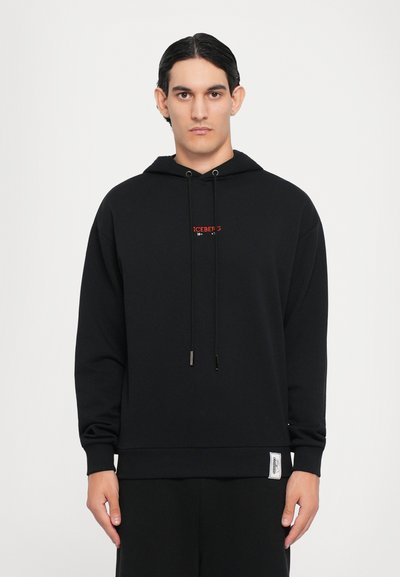 Hoodie noir en tissu doux, avec un cordon de serrage, petit logo rouge sur la poitrine, et une étiquette de marque sur le côté.