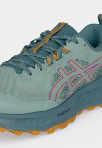 Chaussure de running bleu clair et bleu sarcelle avec des accents orange, logo ASICS, tige en mesh texturé, lacets à motifs et semelle Amplifoam+.