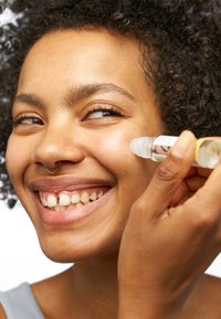 Sérum clair dans un flacon roller transparent appliqué sur un visage souriant. La peau a une texture lisse, avec un éclat naturel et de légères taches de rousseur.