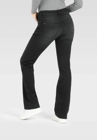 Svarte flared jeans laget av denim, med to baklommer og en jevn tekstur. Kombinert med hvite joggesko, som viser en avslappet passform.