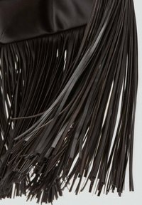 Détail de franges noires sur un fond de tissu lisse, présentant des bandes longues et étroites qui créent une texture en couches.