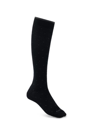 Une seule chaussette noire haute jusqu'au genou avec un motif à pois subtil sur fond blanc.