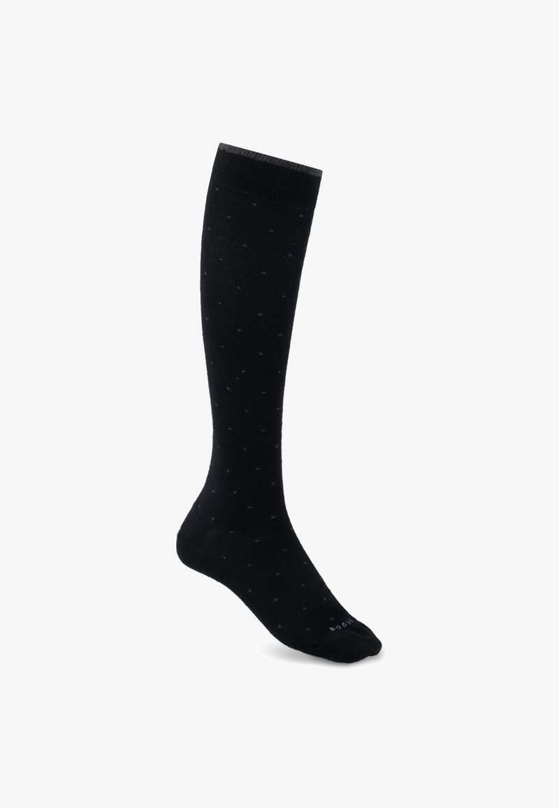 Une seule chaussette noire haute jusqu'au genou avec un motif à pois subtil sur fond blanc.