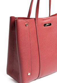 Rote Ledertasche mit strukturierter Oberfläche, zwei Griffen, goldfarbenen Beschlägen und einer dekorativen Logo-Plakette auf der Vorderseite.