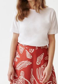 Top bianco a maniche corte abbinato a una gonna rossa con un motivo a foglie bianche, che mette in mostra un tessuto liscio e un design in vita aderente.