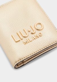 Portafoglio in pelle con texture dorata, con il nome del marchio "LIU·JO MILANO" in metallo lucido impresso. Presenta un design pieghevole e bordi lisci.